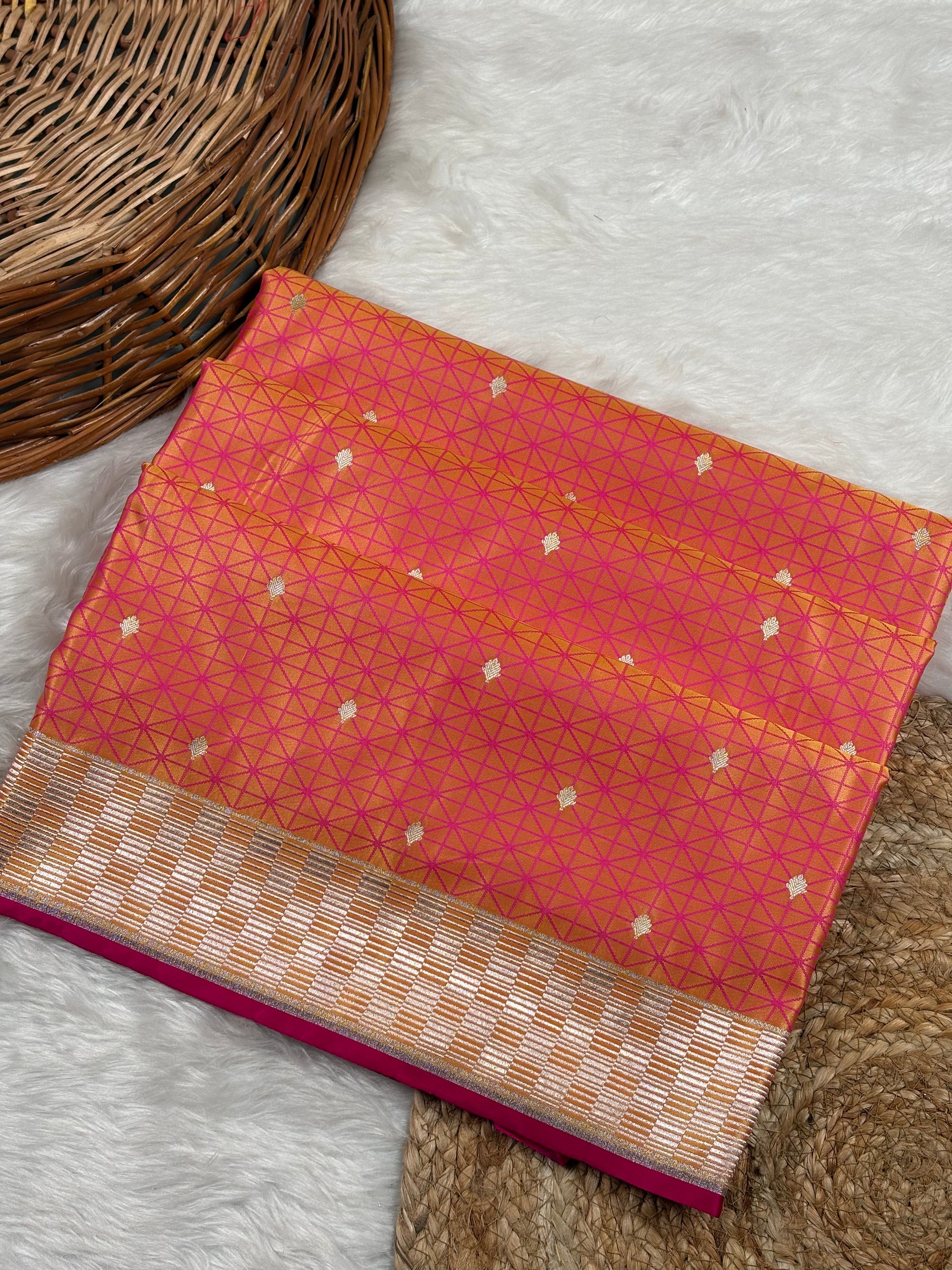 A folded pink and orange silk saree with gold zari geometric tanchui patterns and a metallic gold border weaving, displayed on a white faux fur rug next to a woven wicker basket.
