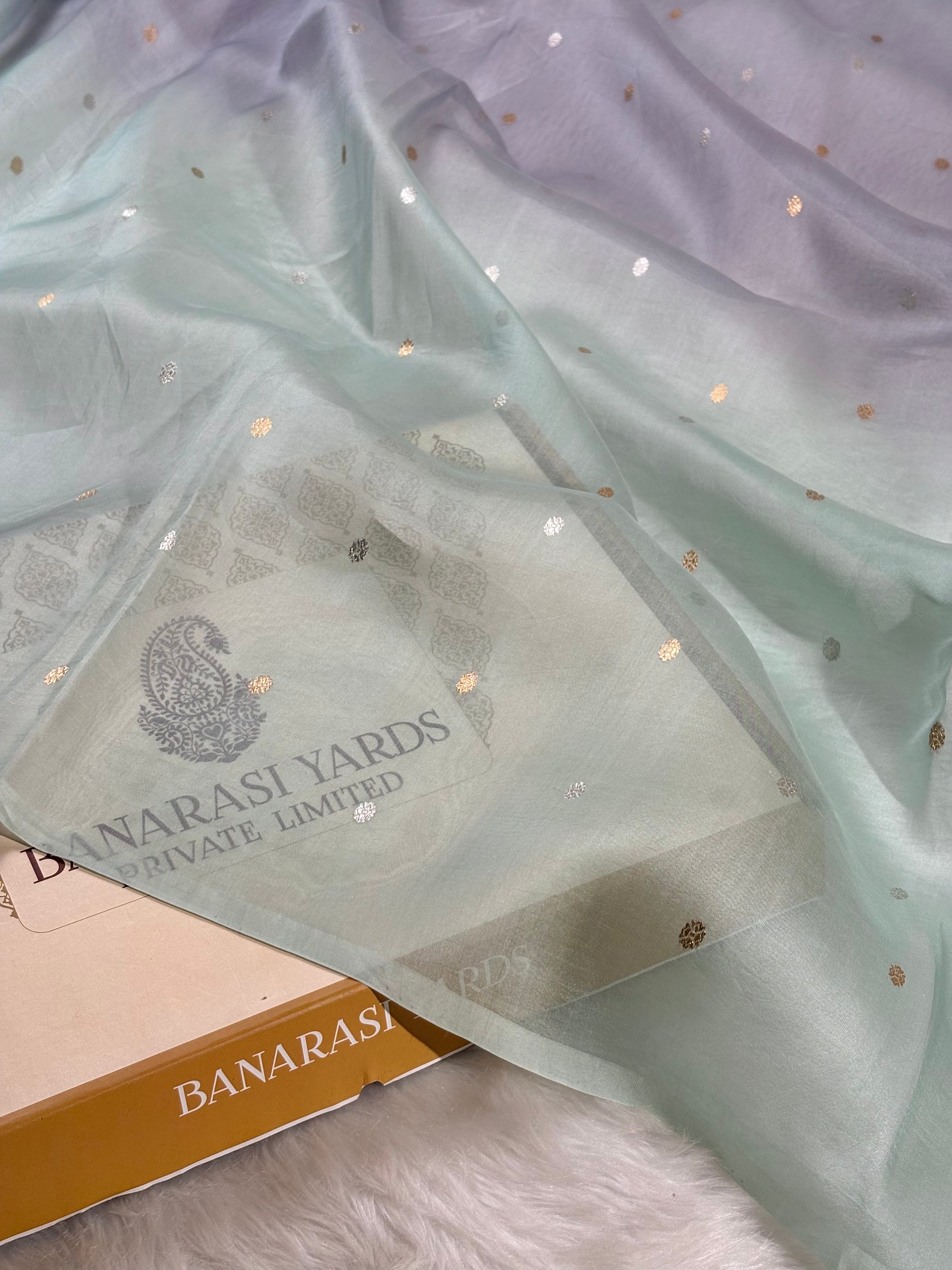A sheer mint green organza with scattered gold foil dots, draped over a light box labeled 'BANARASI YARDS PRIVATE LIMITED'.
