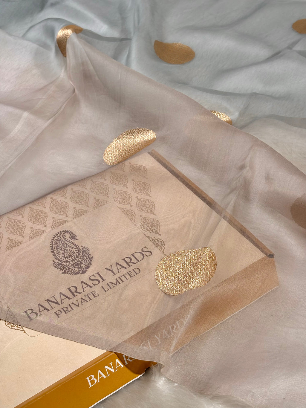 pure kora organza silk saree with a decorated with gold polka dots, draped over its branded packaging box.