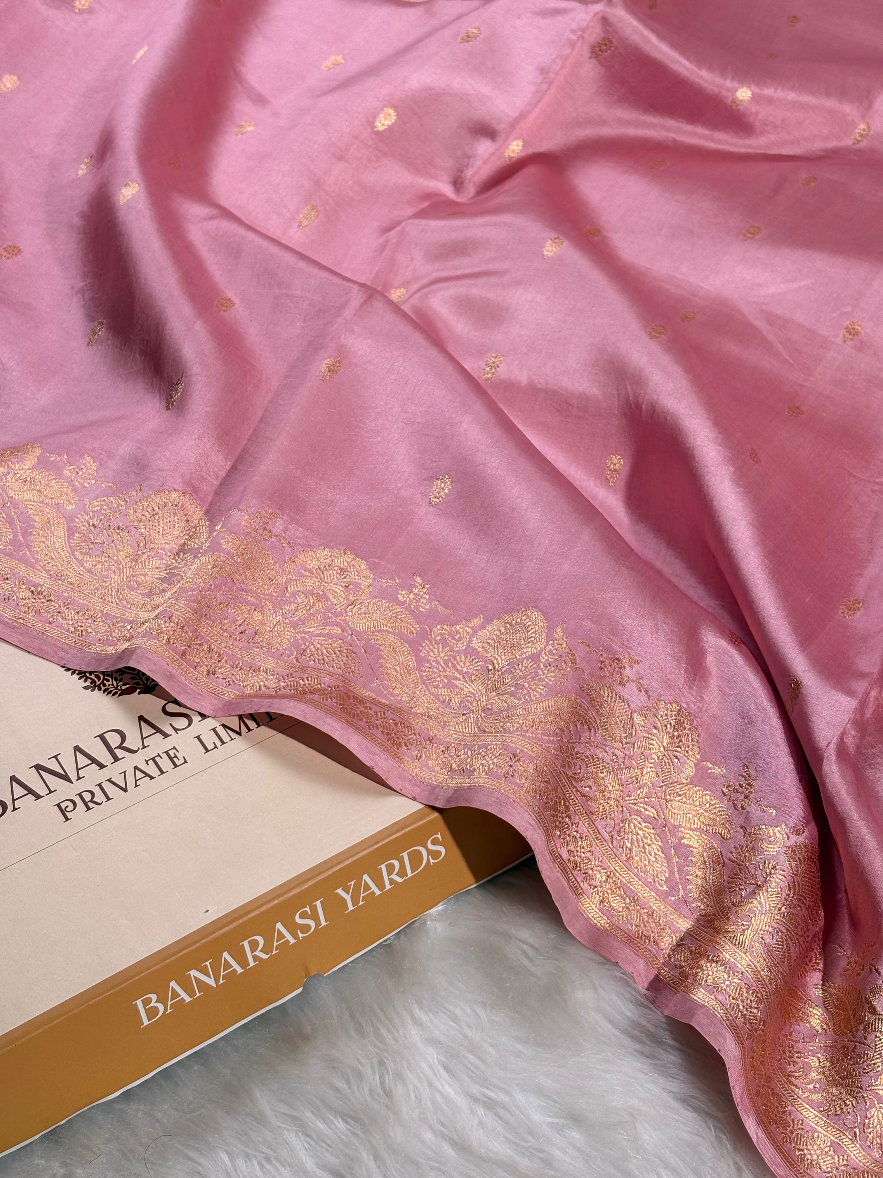pure katan silk handloom Banarasi saree with a gold zari border and small gold motifs, draped over a box labeled 'BANARASI YARDS' on a white faux fur surface.