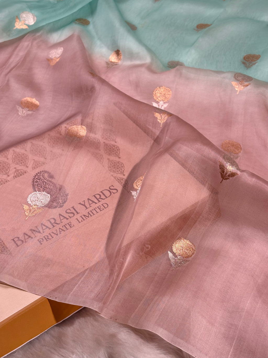 A sheer dusty pink organza saree with metallic rose gold foil motifs and ombre dye. The brand name 'BANARASI YARDS PRIVATE LIMITED' is printed box