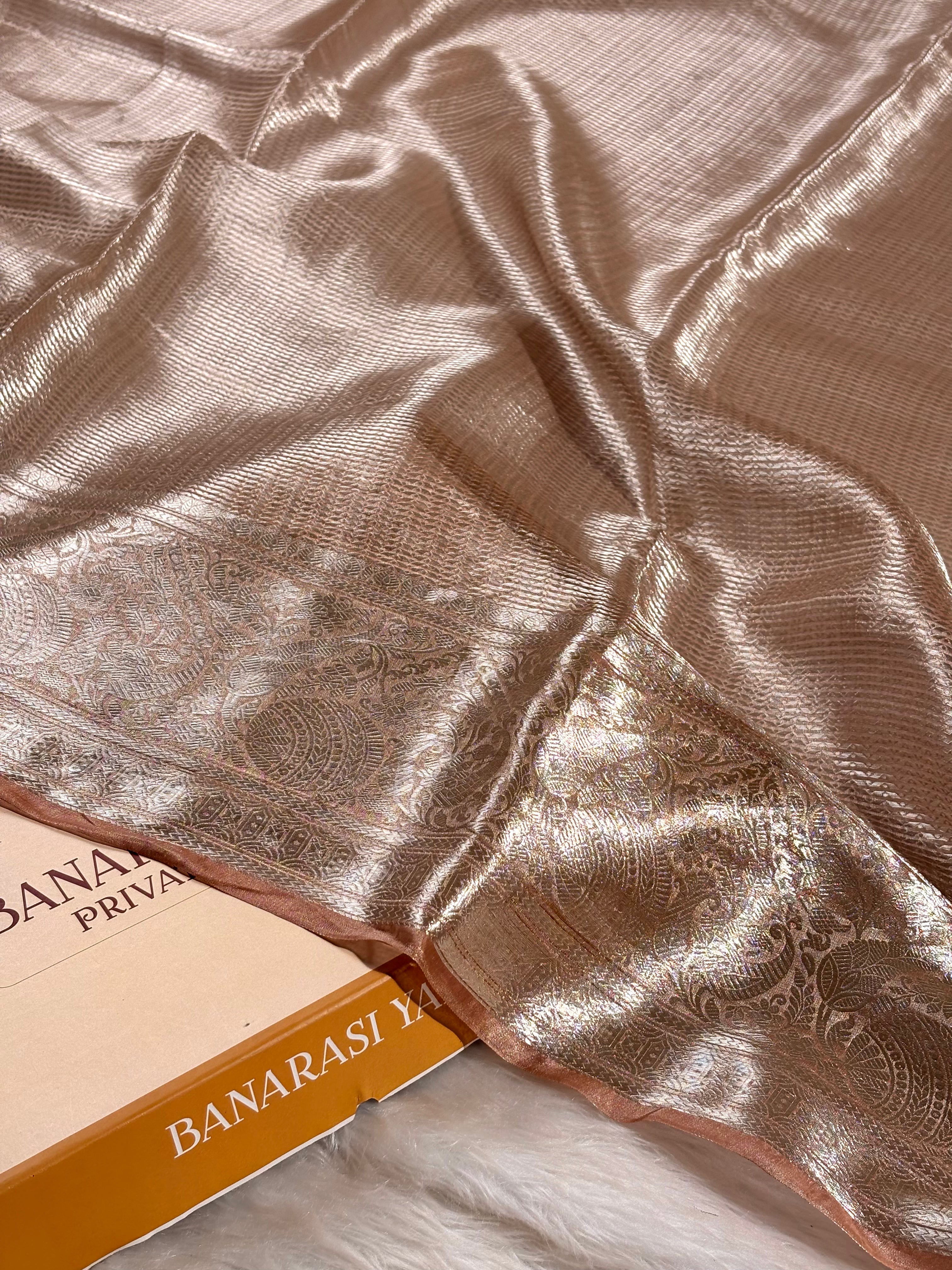 Pure molten tishu silk metallic rose gold saree with a woven paisley border, laid flat on a white faux fur surface.