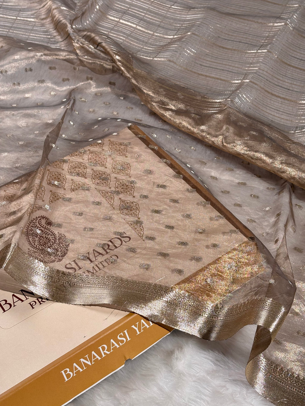 pure tishu silk saree with a metallic gold border, draped elegantly over a white faux fur surface.