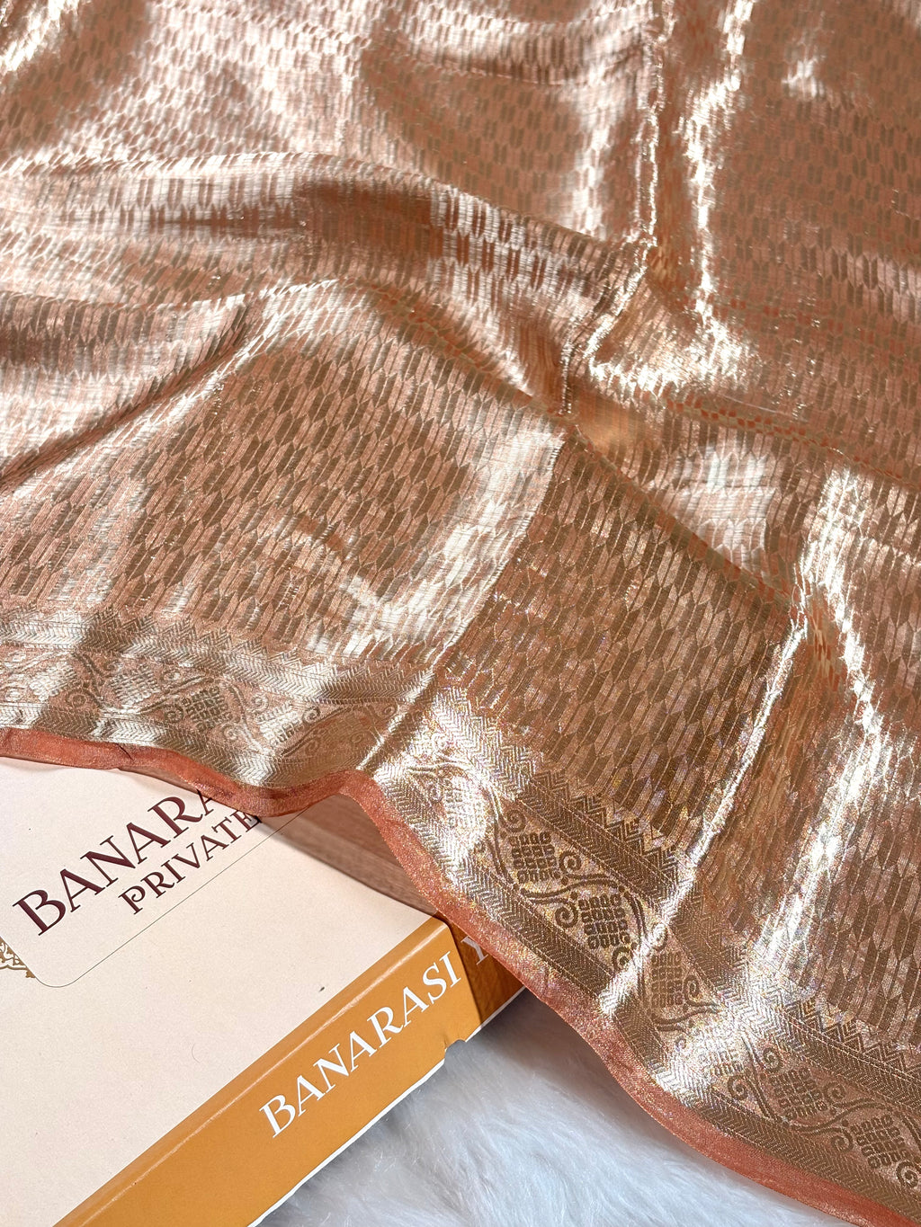 A close-up of a metallic copper-brown saree with an intricate woven floral pattern and a shimmering border.