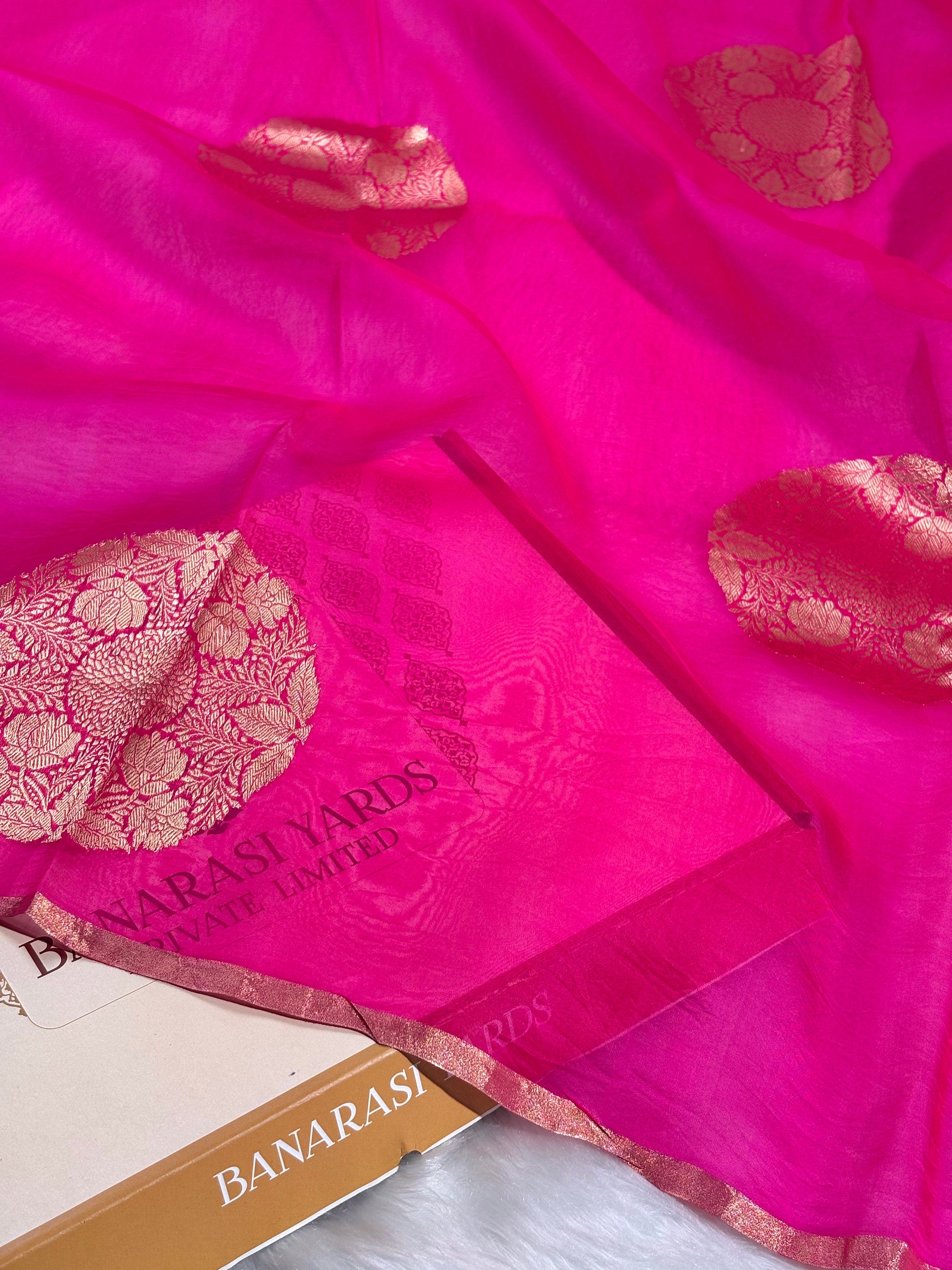 Bright pink Banarasi silk saree with gold zari motifs and a displayed with a Banarasi Yards box.