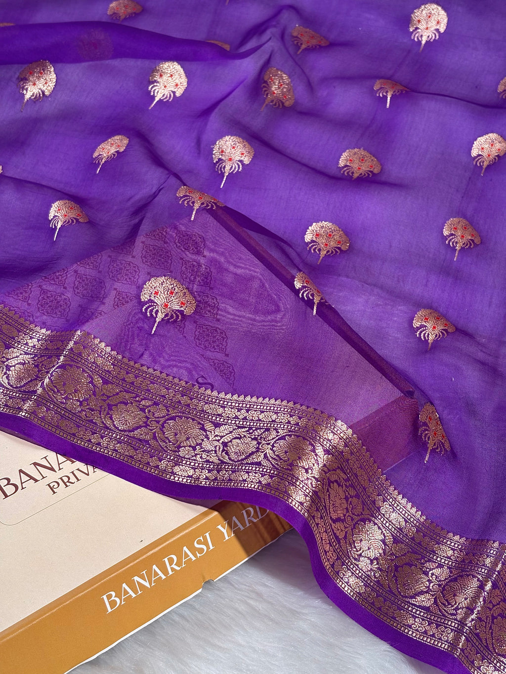 Crafted on traditional handlooms in Varanasi, this Pure Kora Organza Banarasi saree combines delicate transparency with timeless elegance. The sheer organza weave creates a luminous drape, while intricate mina work adorns the fabric in rich red tones, bringing depth and sophistication to every wear.
